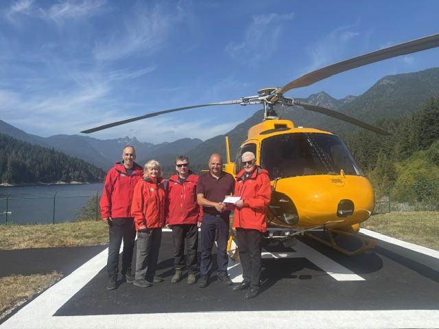 Dan Pistilli with members of North Shore Rescue in front of their yellow rescue helicopter